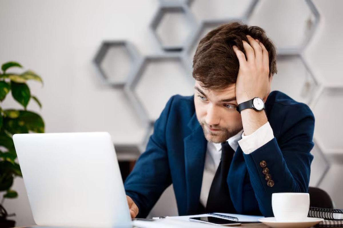 A stressed business owner looking at a laptop with a hand on his head.
