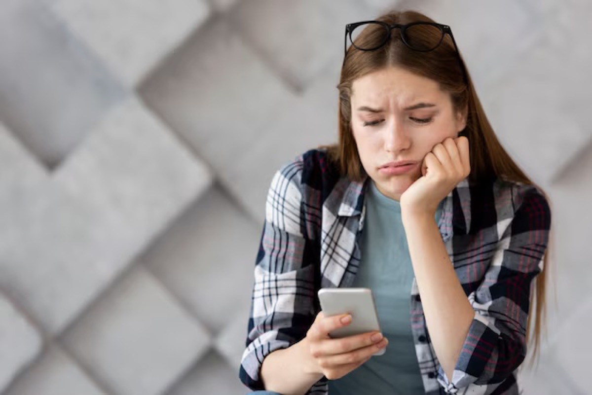 A young woman looking unimpressed at a notification on her phone.