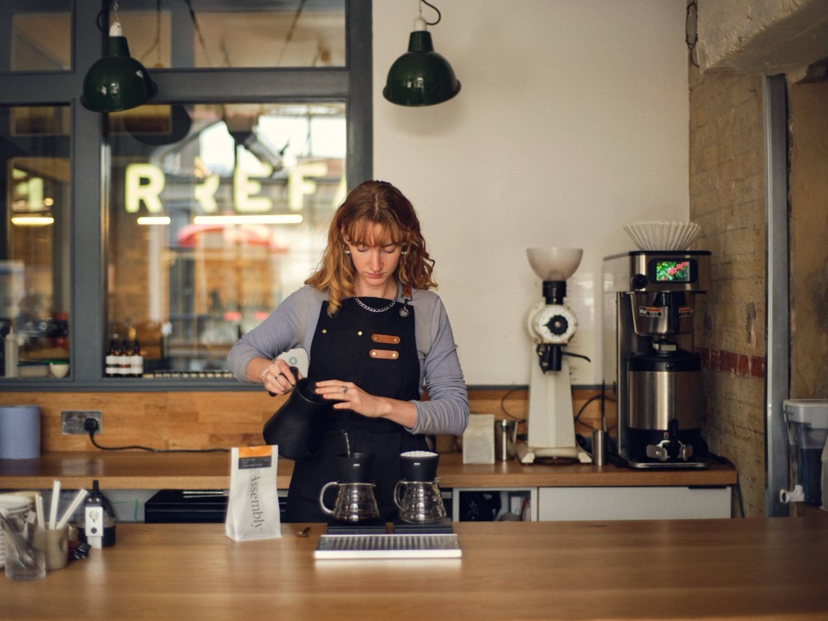 A barista pouring coffee behind a busy café counter.